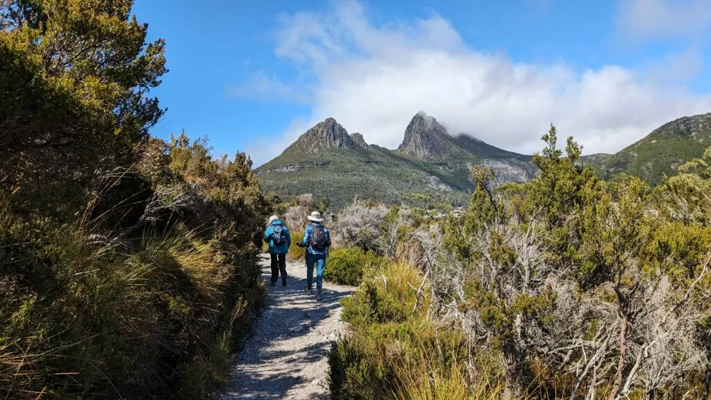 Two hikers walk a gravel track on the Dove Lake Circuit with Cradle Mountain in the background
